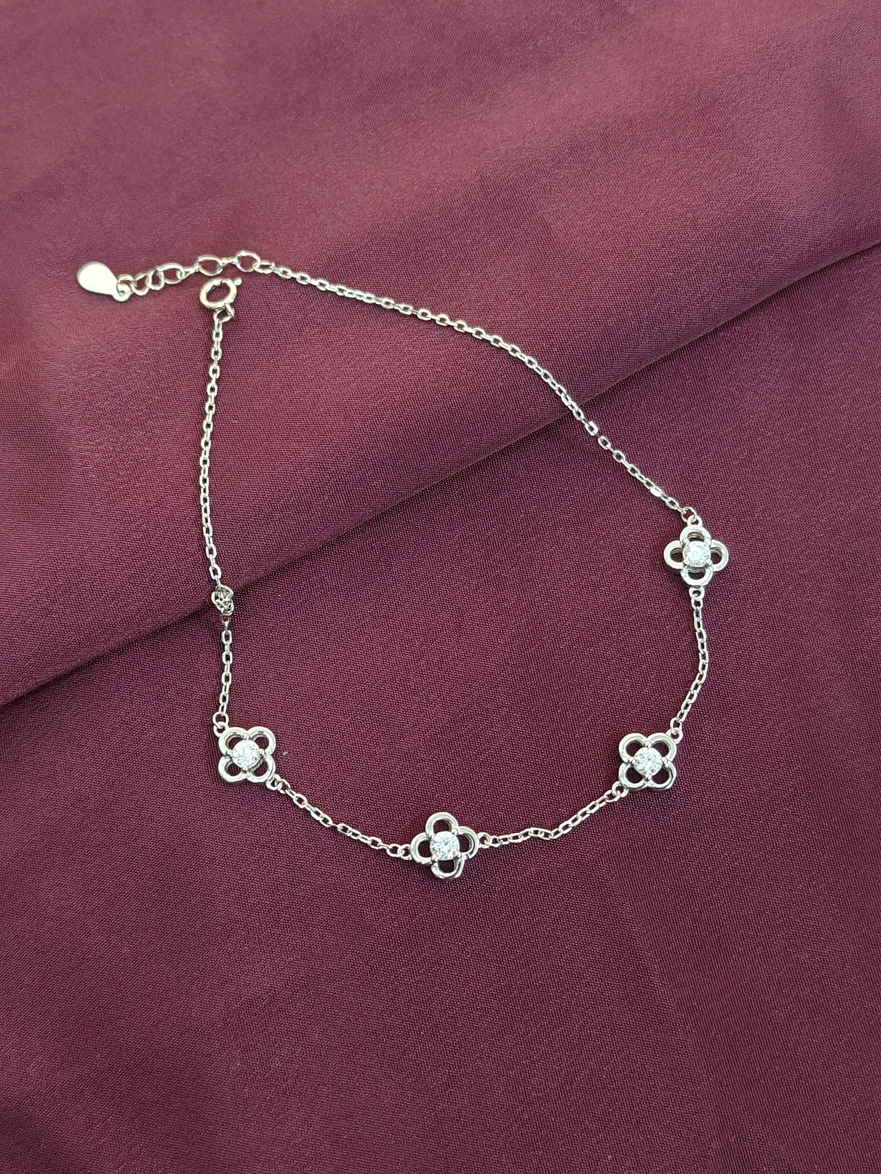 Silver chain bracelet with clover-shaped charms on a purple fabric background